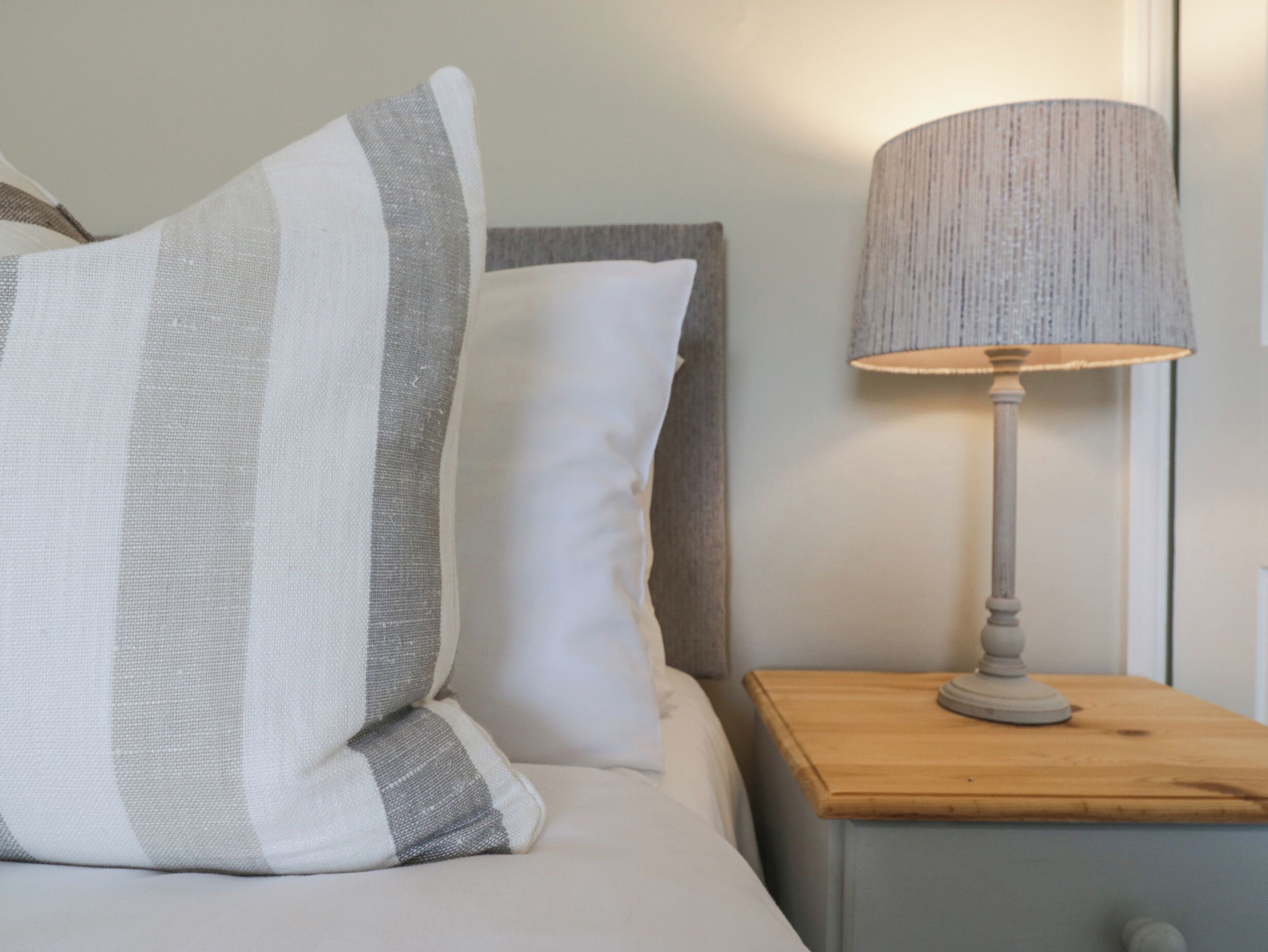 Un lit avec des oreillers à rayures, une lampe de chevet et une table de nuit en bois.