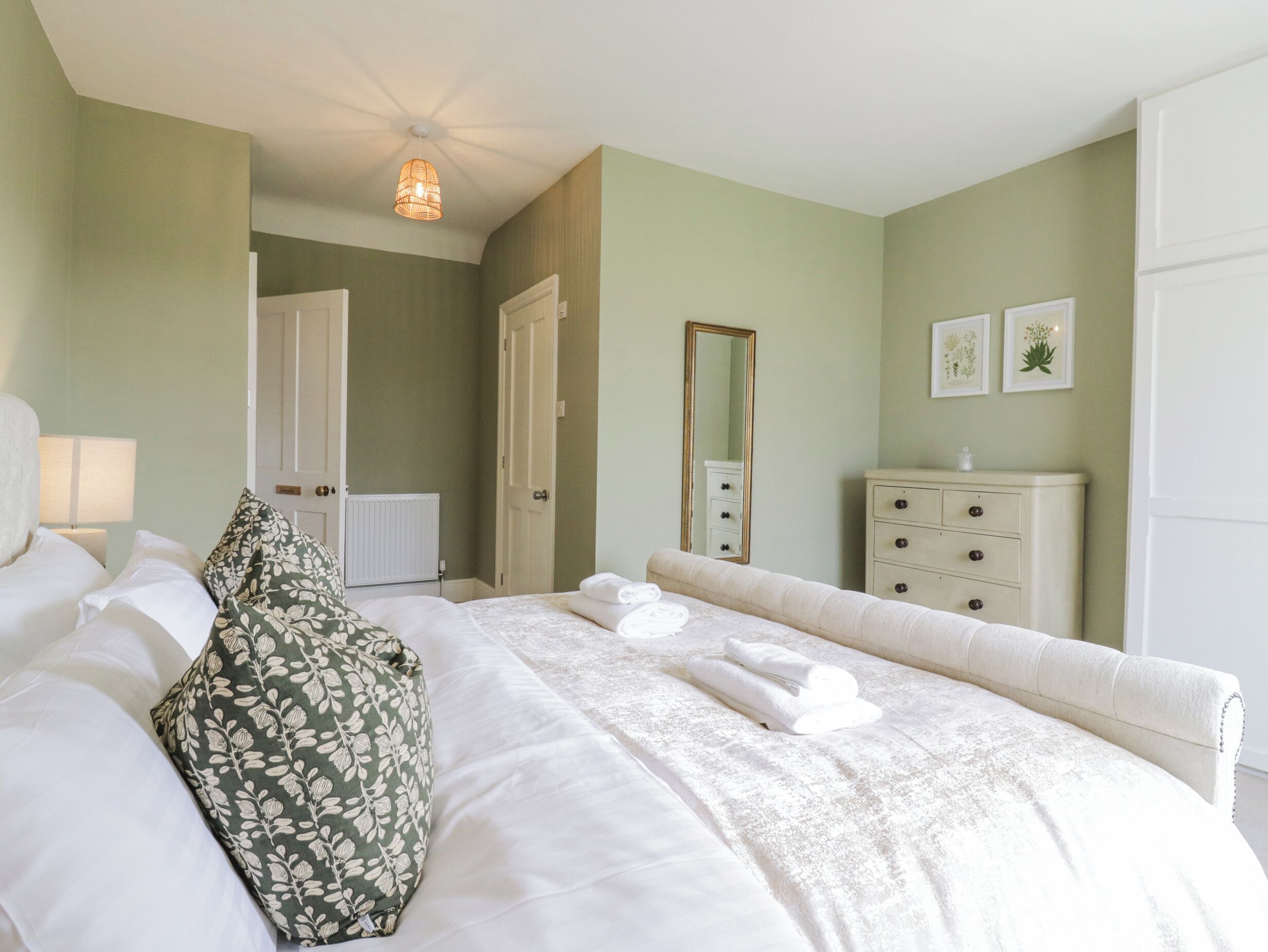 A bedroom with a bed, a dresser, a mirror, and a door leading to another room.