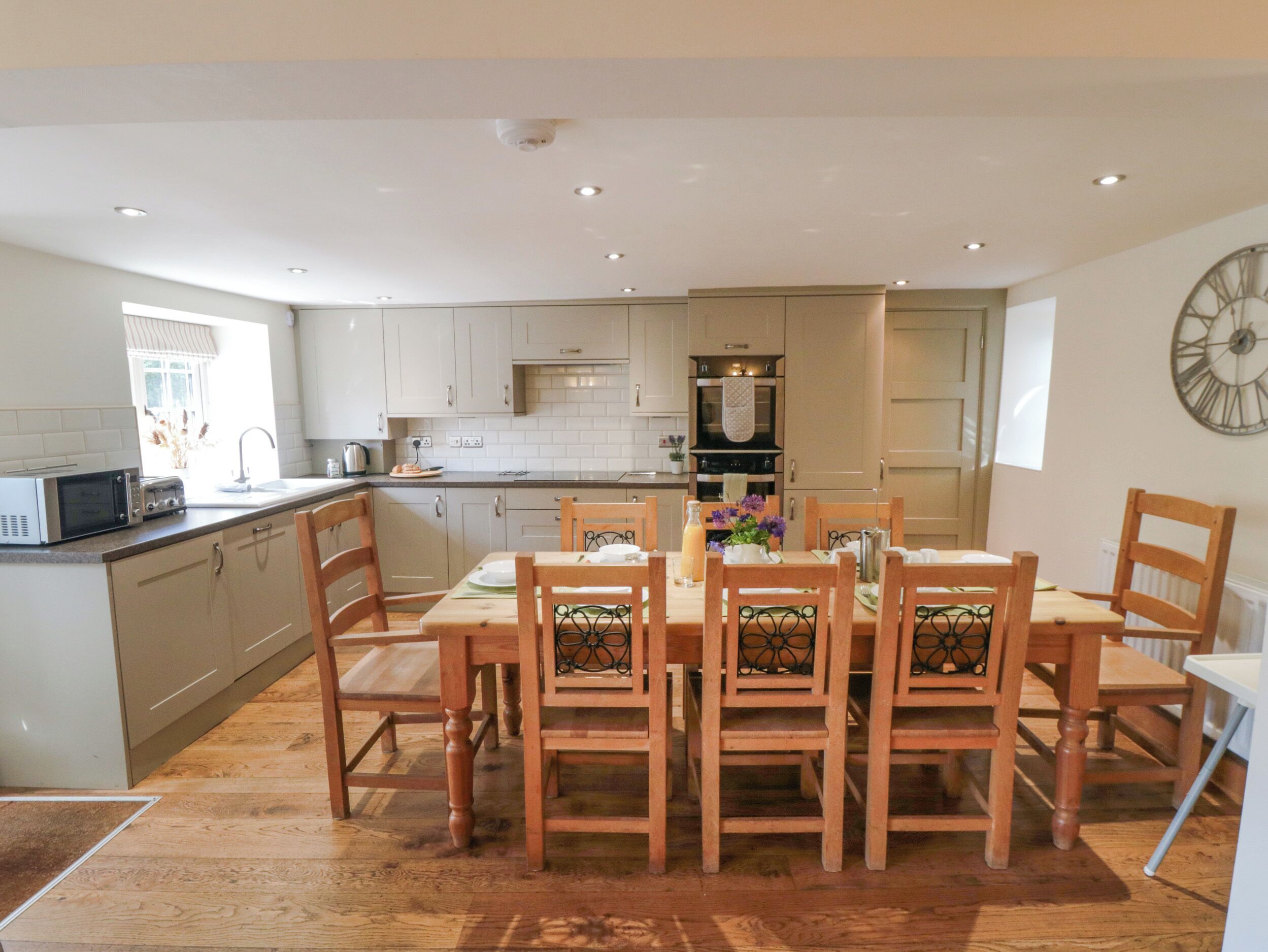 Una cocina moderna con armarios de madera, una mesa de comedor con sillas y un reloj grande en la pared.