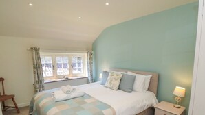 Ein Schlafzimmer mit einem Bett, einem Nachttisch, einem Fenster mit Vorhängen und einem Sessel.
