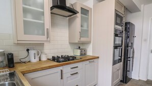 Una cocina con armarios blancos, encimera de madera, cocina a gas, tostadora y refrigerador negro.