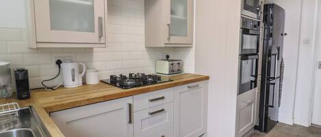 A kitchen with white cabinets, a wooden countertop, a gas stove, a toaster, and a black refrigerator.
