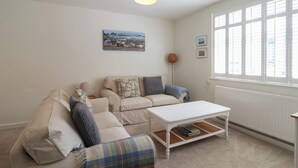 Una sala de estar acogedora con un sofá, una mesa de centro y una lámpara. Hay una ventana con persianas y un cuadro en la pared.