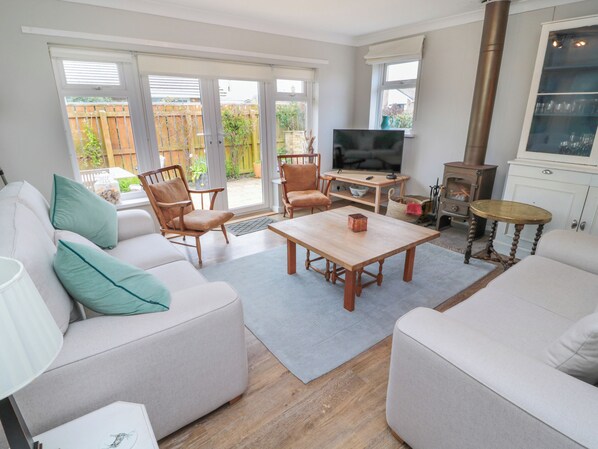 Una sala de estar con sofá, sillones, mesa de centro, televisor, chimenea y vistas al exterior.