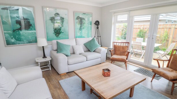 Una sala de estar moderna con un sofá blanco, una mesa de centro de madera y un ventanal con vista al patio trasero.