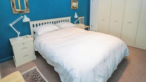 Un dormitorio con cama, mesita de noche, escritorio, silla, armario y espejo en la pared.