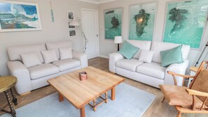Una sala moderna con dos sofás blancos, una mesa de centro de madera y un sillón de madera.