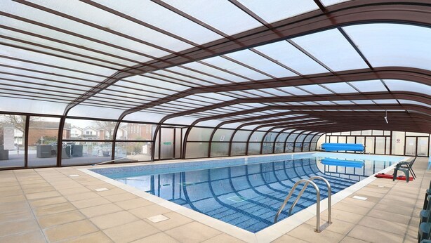 Une piscine intérieure dotée d’un toit en verre, d’un sol carrelé et d’une zone de piscine aux couleurs bleues.