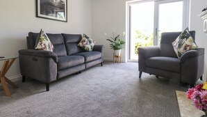 En stue med en grå sofa, en grå lænestol og en potteplante.