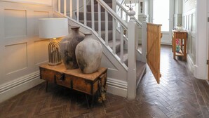 Una escalera con barandillas blancas, un banco de madera con dos jarrones y una lámpara colgante.