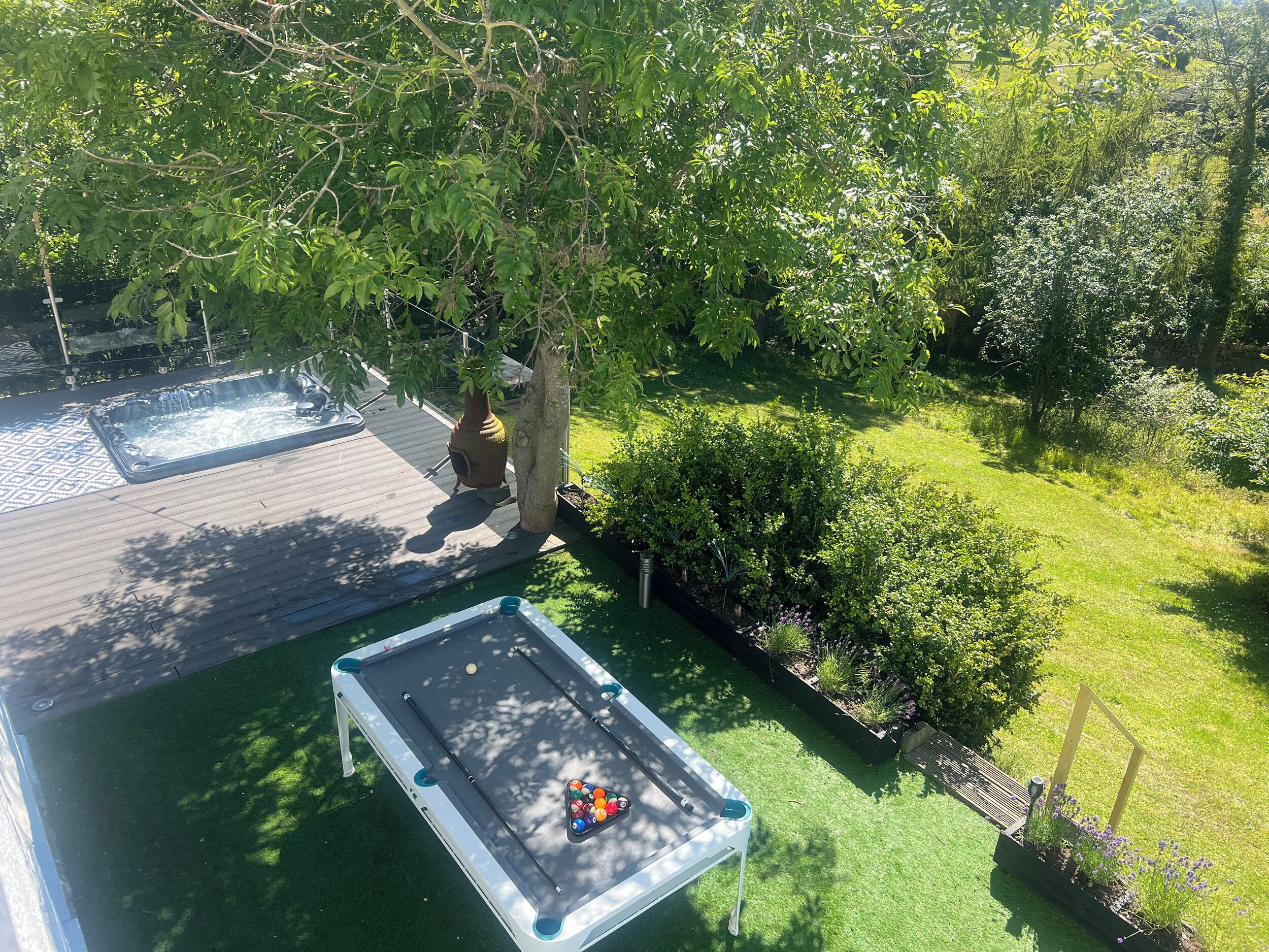 A pool table in a backyard with a hot tub and a wooden deck.