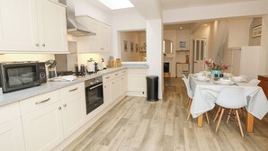 Een moderne keuken met witte kastjes, een magnetron, oven en een eethoek met een tafel voor vier personen.
