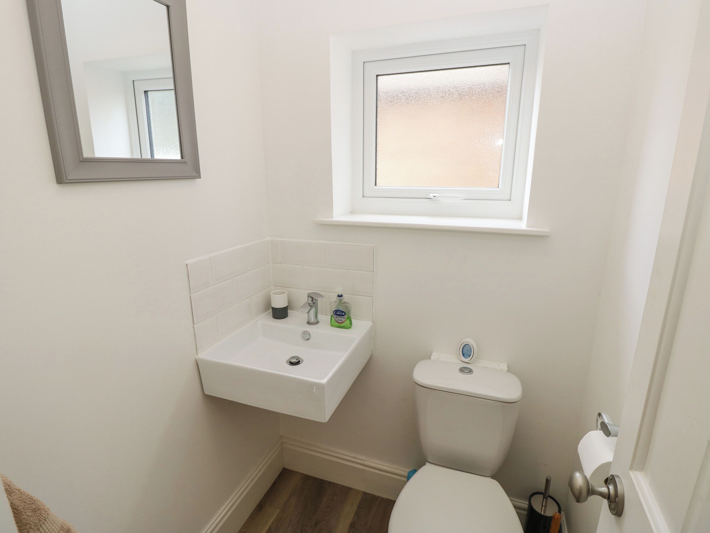 A small, clean bathroom with a white sink, toilet, and a window above the sink.