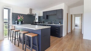 Une cuisine moderne dotée d’un grand îlot central, de meubles de rangement aux couleurs sombres et offrant une vue sur l’extérieur.