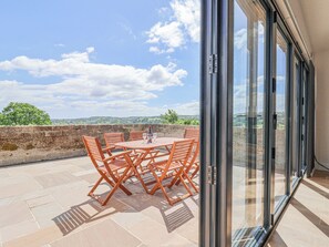 A patio with a table and chairs, a bottle of wine, and a view of the countryside through a glass door. - Pit Close (Honiton)