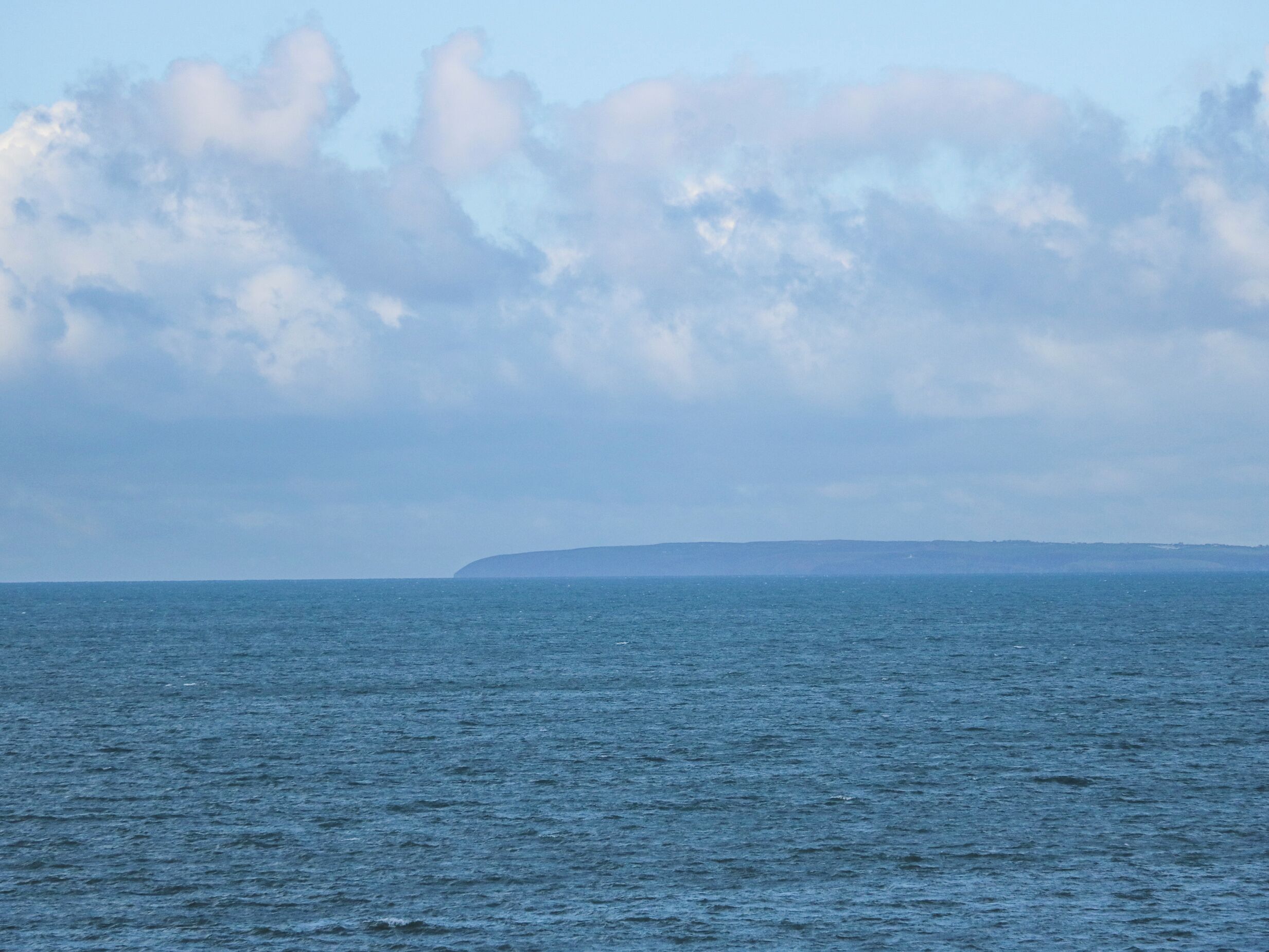 A coastal view with a calm sea and a distant landmass under a cloudy sky.