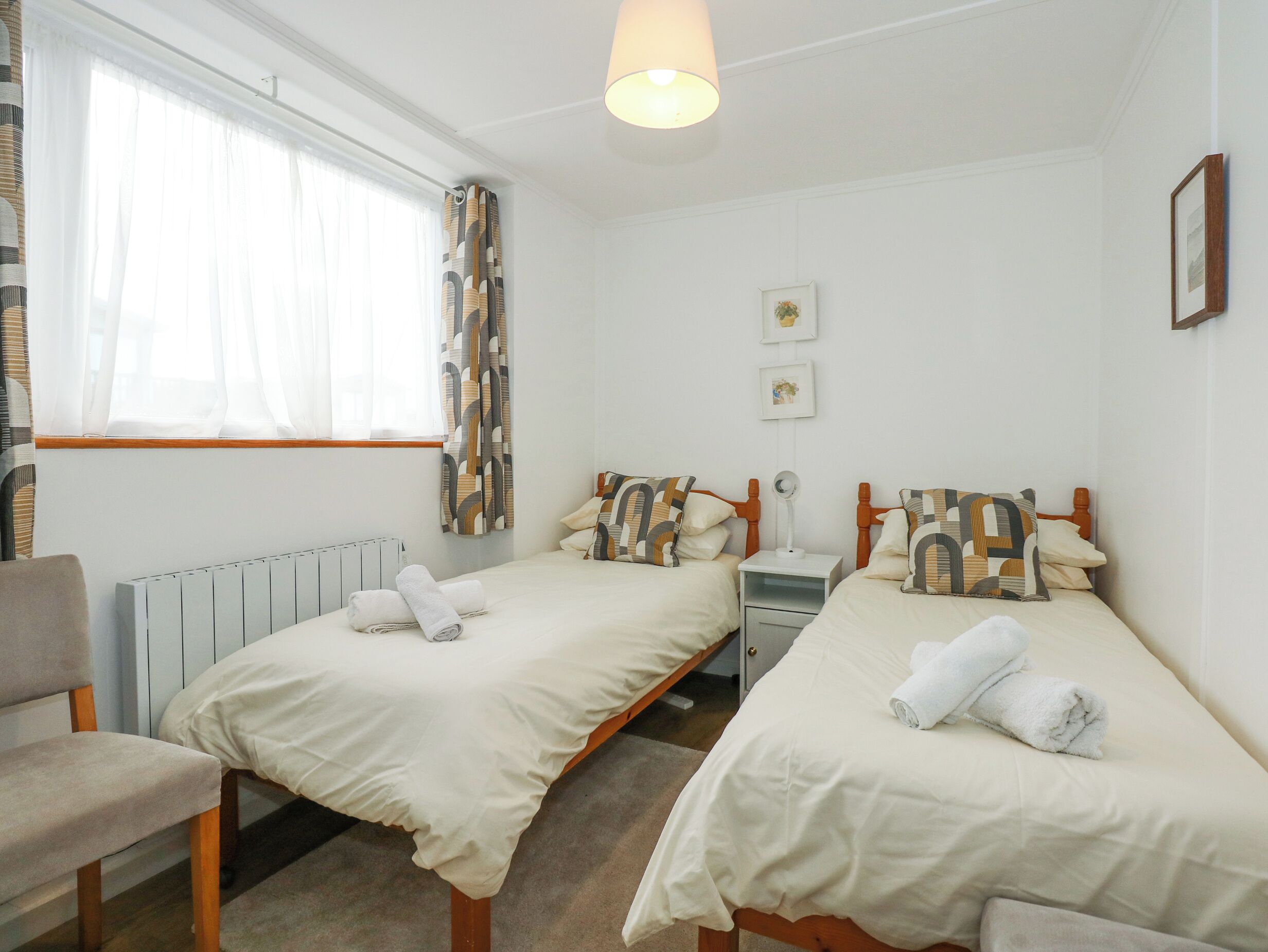 A twin room with two beds, a radiator, a chair, a desk, and a window with curtains.