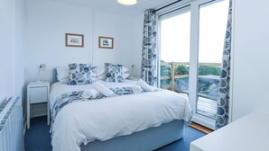 A bedroom with a bed, a nightstand, a lamp, and a window with a view. - Ael Y Don (Harlech)