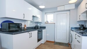 A compact kitchen with white cabinets, a microwave, a coffee maker, and a washing machine. - Ael Y Don (Harlech)