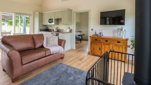 A modern living room with a brown leather sofa, a wooden cabinet, and a flat-screen TV. - Bramble Cottage (Blairgowrie)