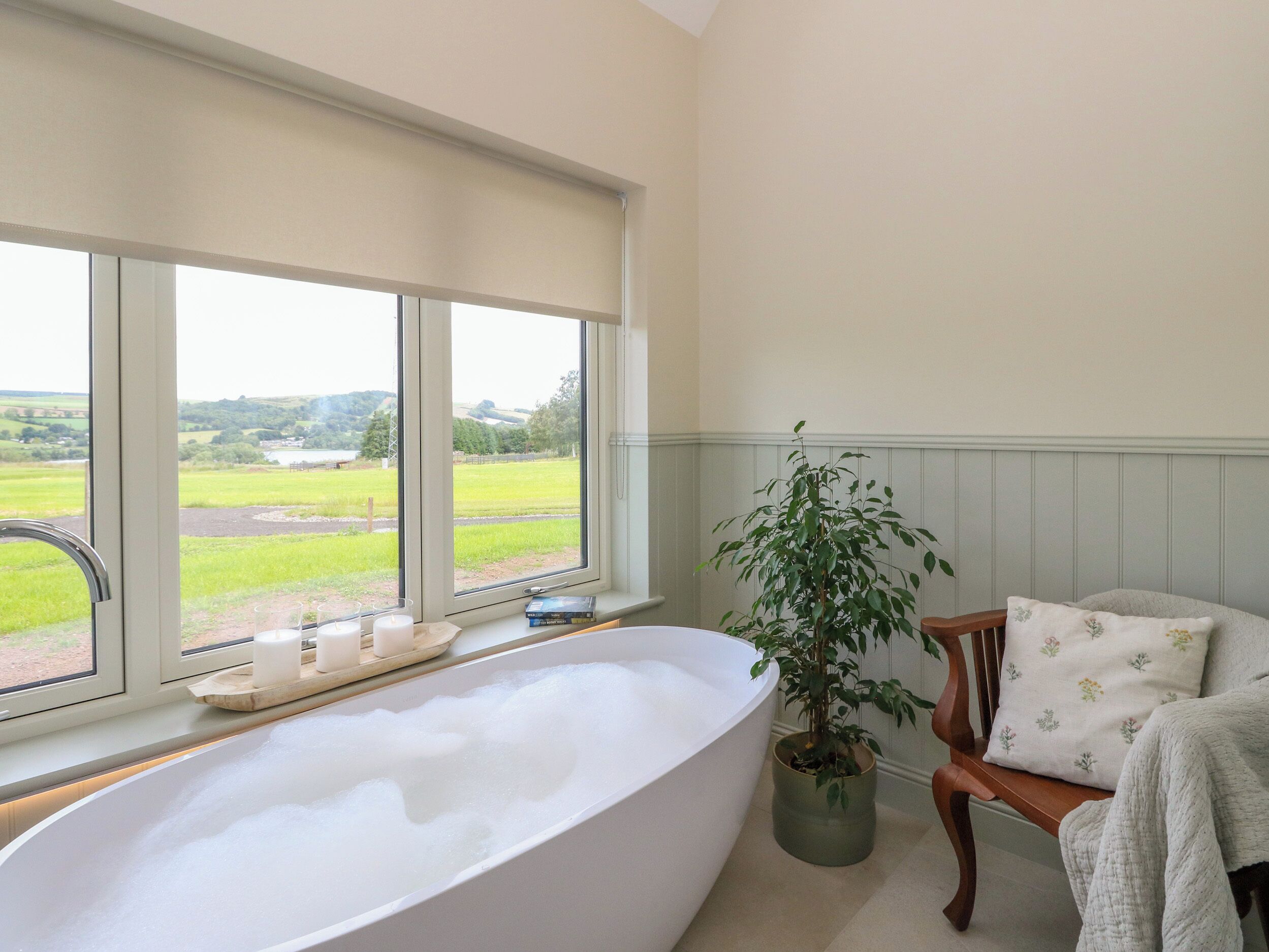Une salle de bain avec une baignoire sur pieds, une plante en pot et une vue sur un paysage verdoyant grâce à de grandes fenêtres.