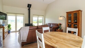 A spacious living area with a large brown leather sofa, a wooden dining table, and a cabinet with glass doors. - Bramble Cottage (Blairgowrie)