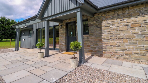 A modern building with a stone facade, large windows, and a covered patio area with potted plants. - Bramble Cottage (Blairgowrie)