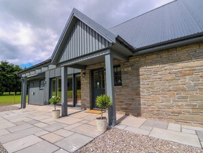 A modern building with a stone facade, large windows, and a covered patio area with potted plants.