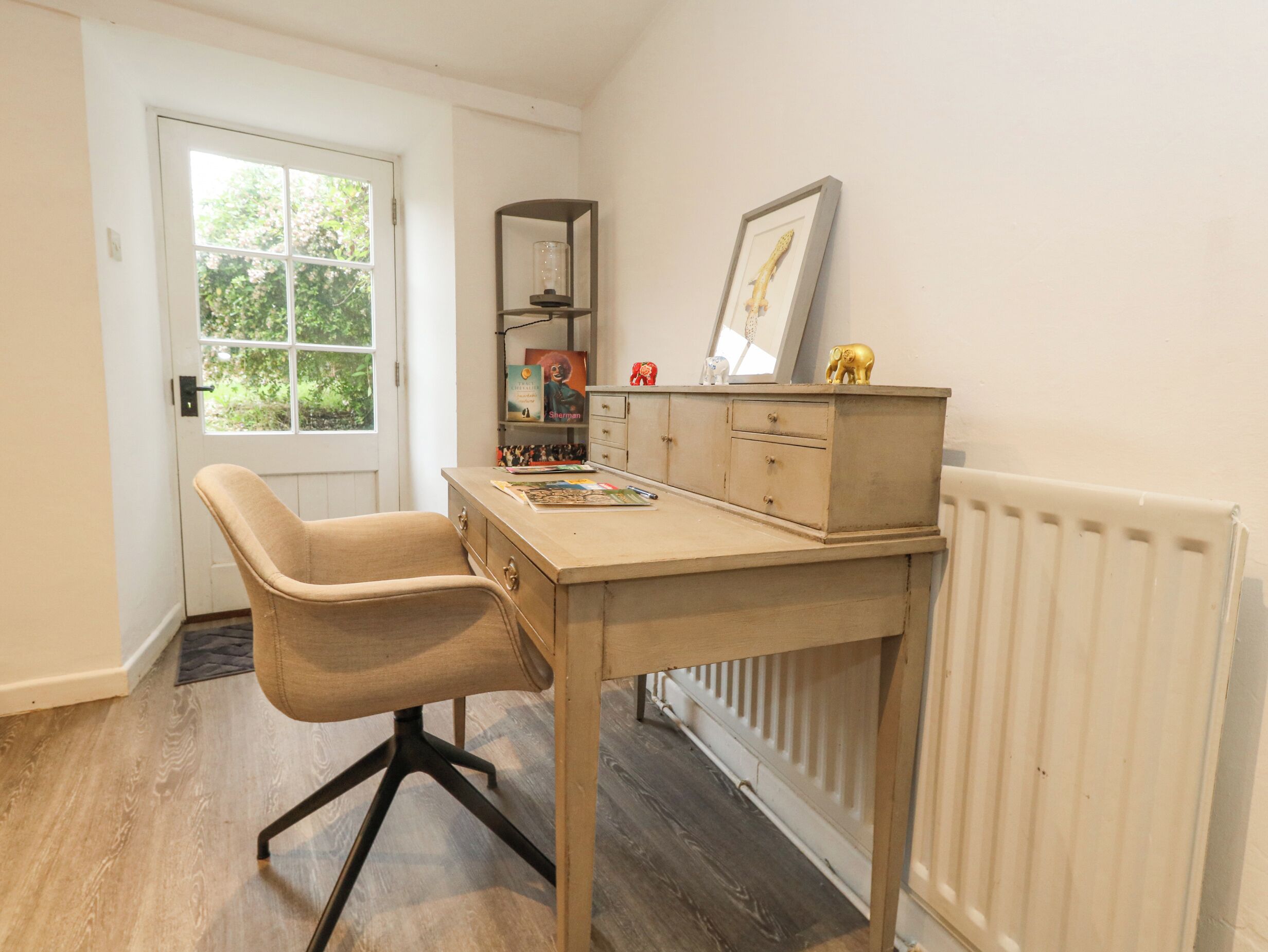 A room with a desk, chair, radiator, and a window with a view of greenery.