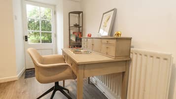 A room with a desk, chair, radiator, and a window with a view of greenery.