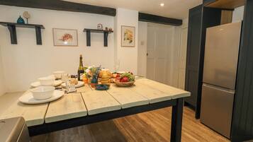 A kitchen with a wooden table set for a meal, a refrigerator, and wall-mounted shelves with decorative items.