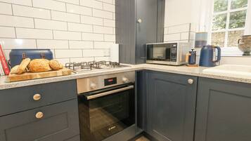 Uma cozinha moderna com armários escuros, um forno Bosch, micro-ondas e fogão a gás.