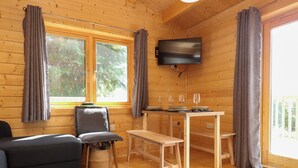 Ein gemütliches Blockhaus-Interieur mit einer Couch, einem Sessel, einem Esstisch mit Weingläsern und einem an der Wand befestigten Fernseher.