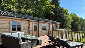 Eine Holzhütte mit einer Terrasse, Korbmöbeln und Blick auf den umliegenden Wald.