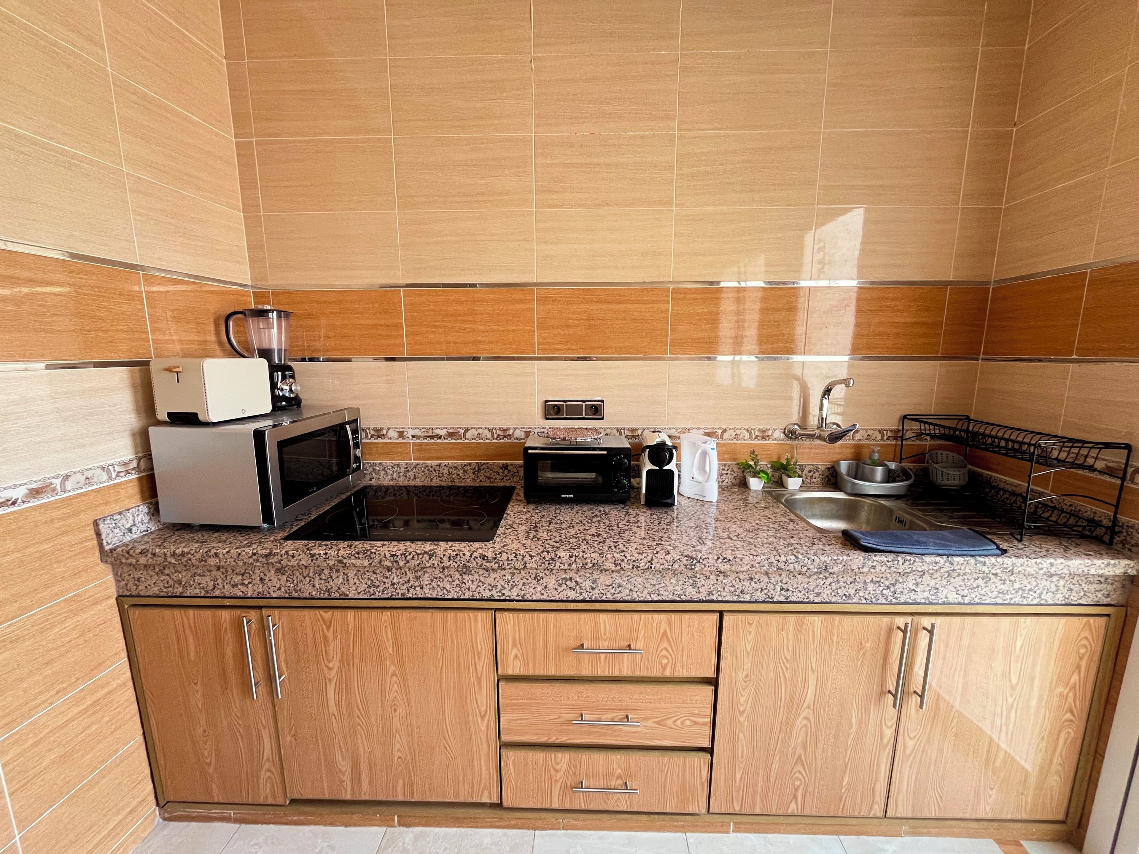 Una cocina equipada con microondas, tostadora, hervidor y pileta.