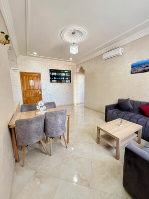 A modern living room with a grey sofa, a wooden coffee table, and a dining area with a table and chairs.
