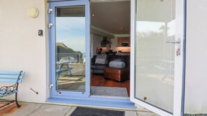 A sliding glass door leading to a living area with a sofa, a table, and a view of the outside. - Apartment 2 (Newquay)