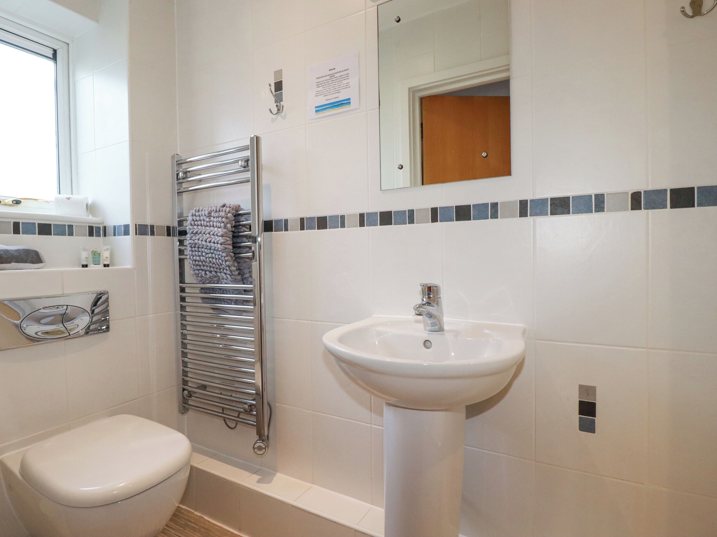 Un baño con inodoro blanco, lavamanos y un perchero para toallas.
