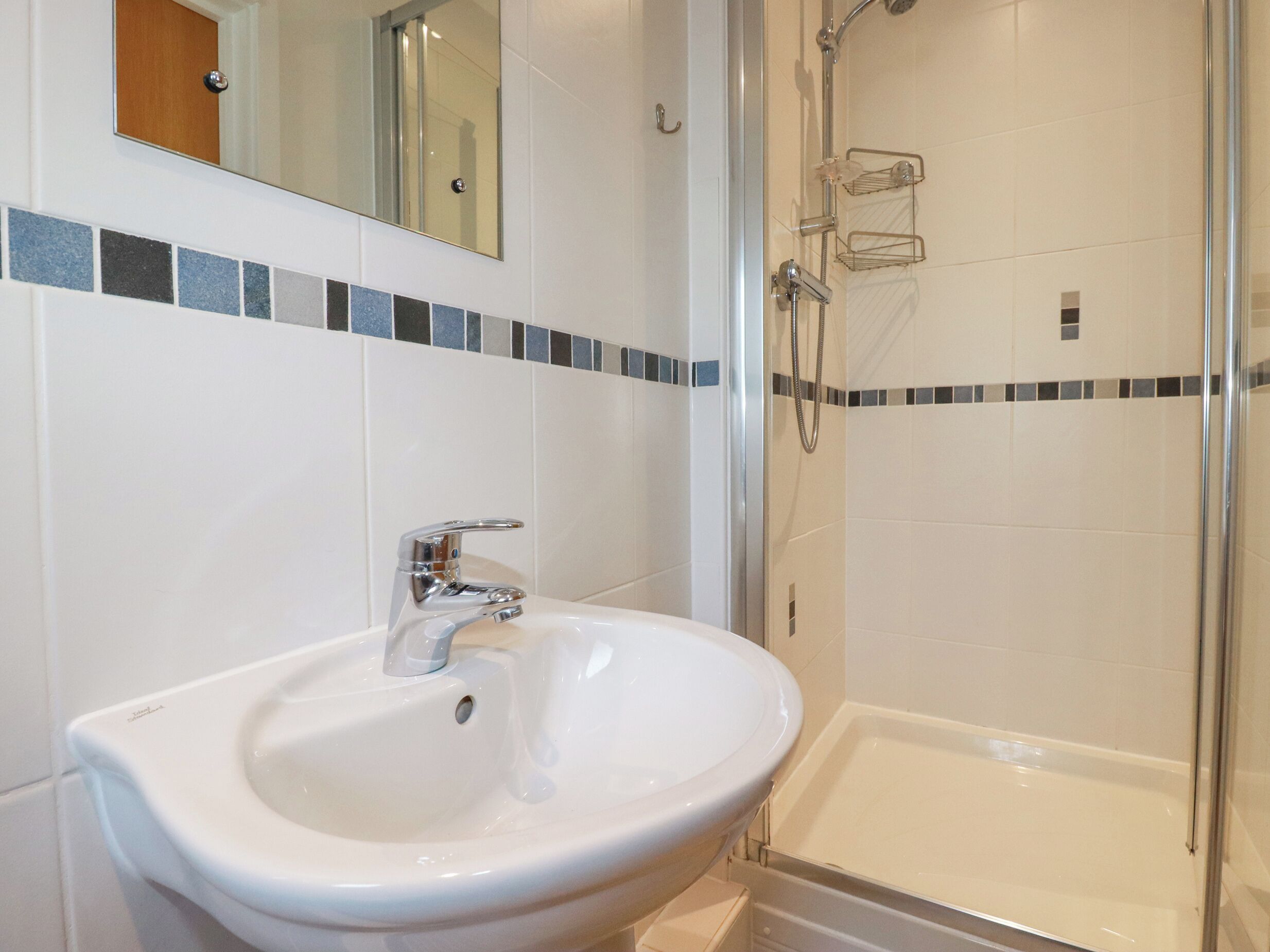 A bathroom with a white sink, a mirror, and a glass-enclosed shower.