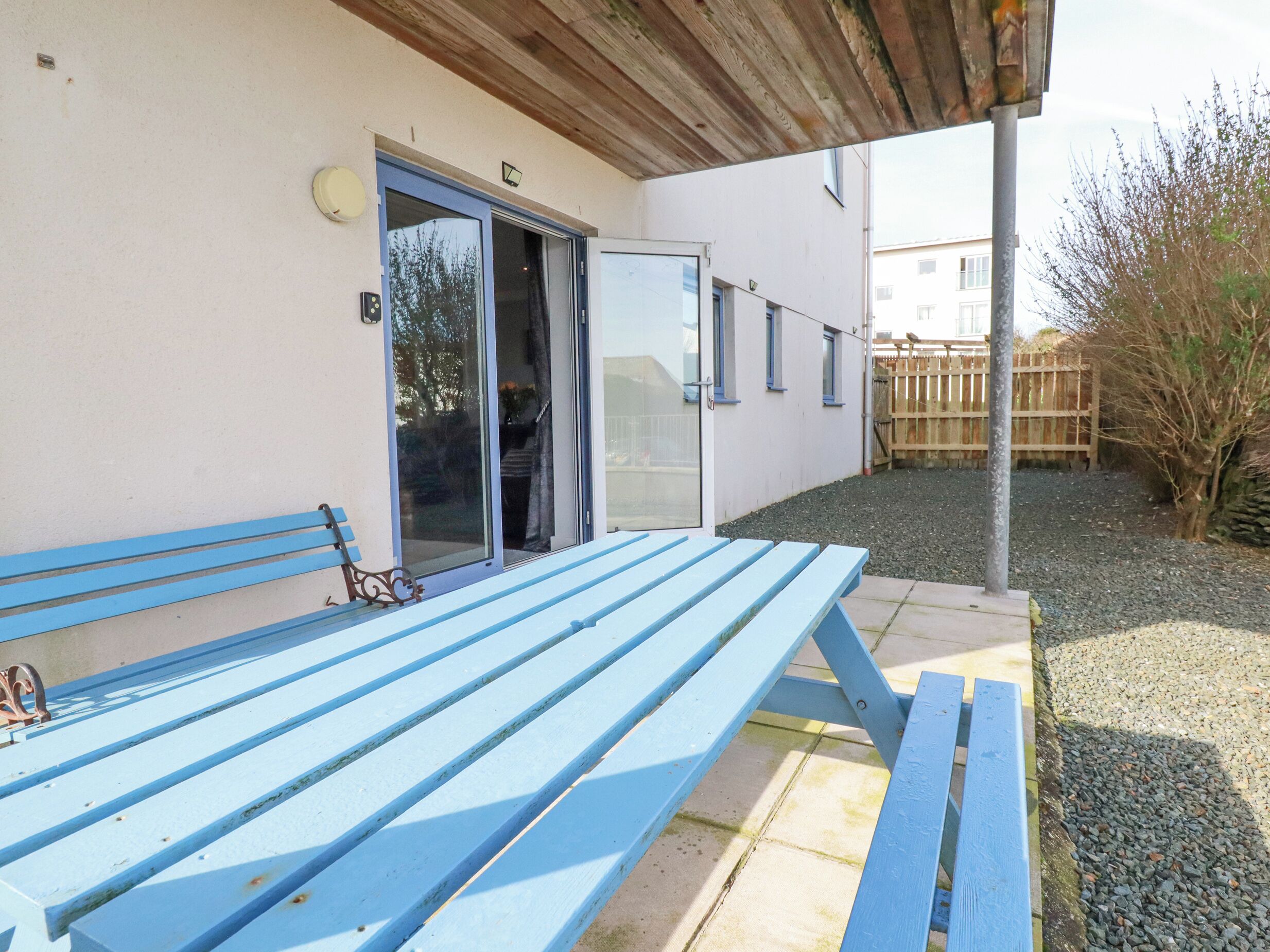 A covered patio with a blue bench, a sliding glass door, and a gravel area.