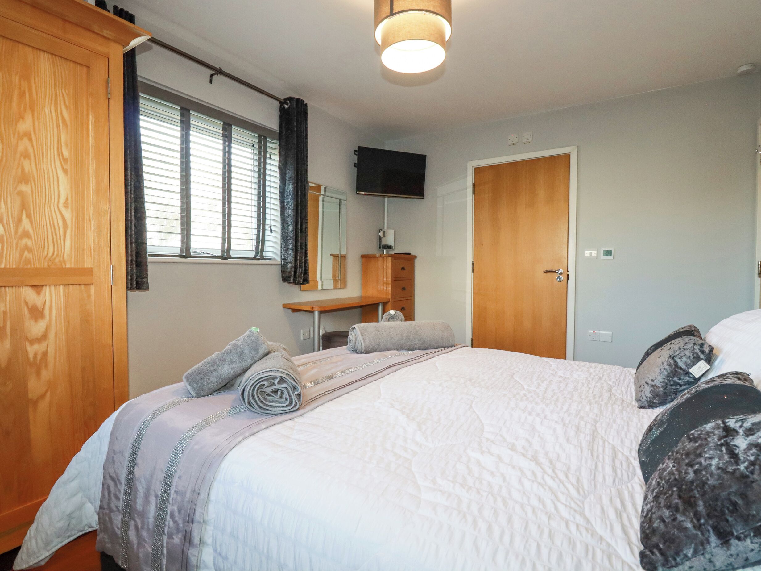 Un dormitorio con una cama grande, un armario de madera, un espejo, un televisor y una ventana con persianas.
