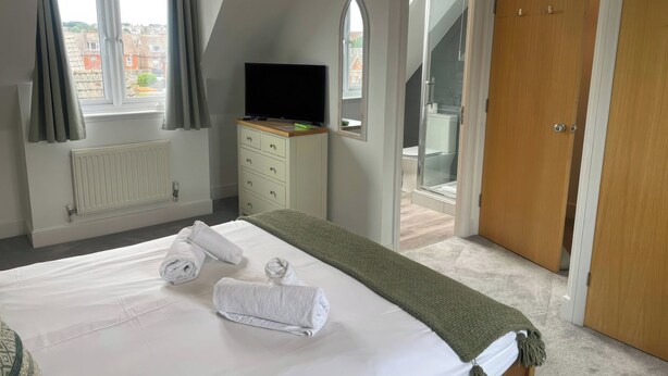Ein Schlafzimmer mit Bett, Fernseher, Heizkörper, Fenster und einer Tür, die auf einen Balkon führt.