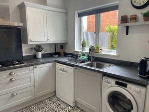 A modern kitchen with white cabinets, a built-in dishwasher, a gas stove, and a window with a view of a brick wall and greenery outside.