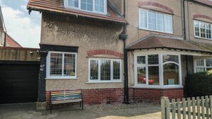 Une maison à deux étages avec un garage, une clôture en bois et un banc à l’extérieur.