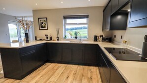 A modern kitchen with dark cabinetry, a large island, and a view of the outdoors. - Pen-y-ghent (Carnforth)