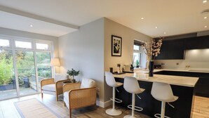 A modern kitchen with a central island, bar stools, and a dining area with wicker chairs. - Pen-y-ghent (Carnforth)
