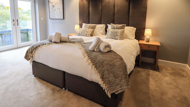 A modern bedroom with a large bed, bedside lamps, and a view of the outdoors through a sliding door. - Pen-y-ghent (Carnforth)