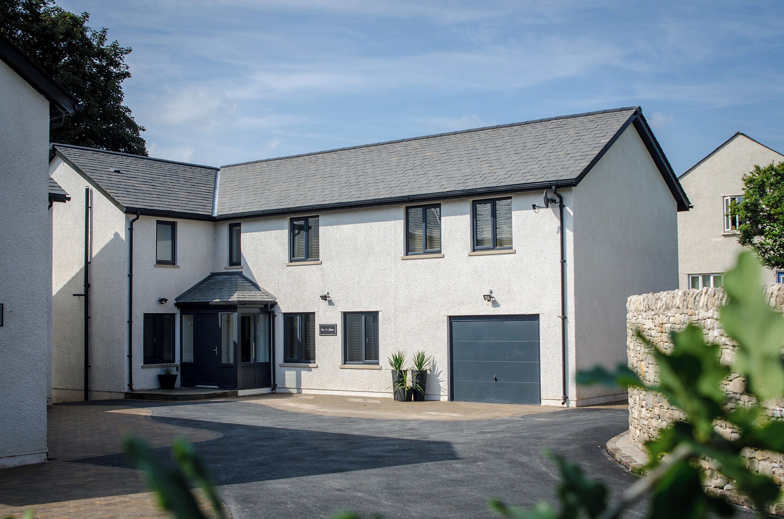 A two-story building with a grey roof, a central entrance, and a garage door.