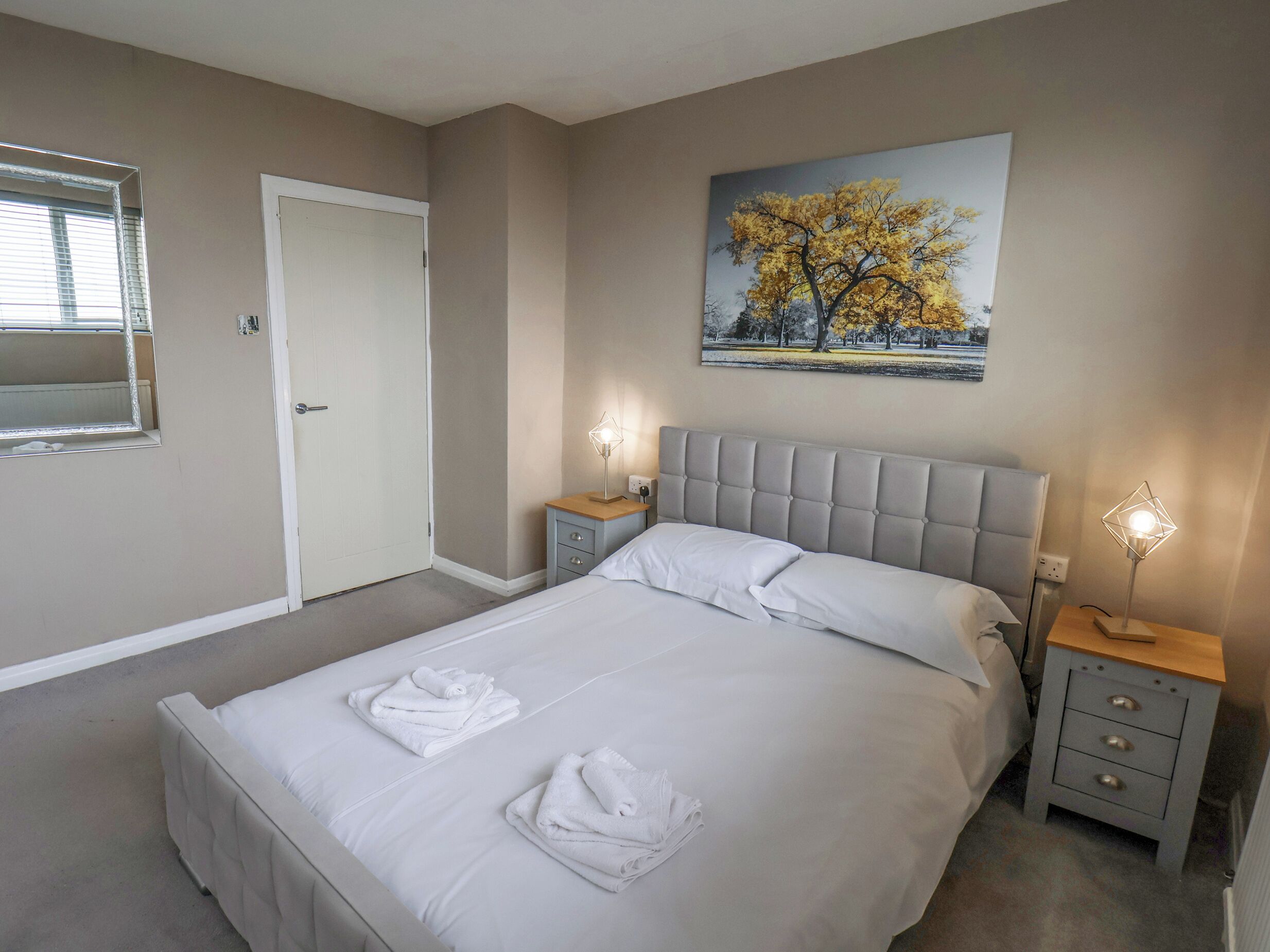 A bedroom with a bed, two bedside tables, a door, and a painting on the wall.