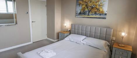 A bedroom with a bed, two bedside tables, a door, and a painting on the wall.
